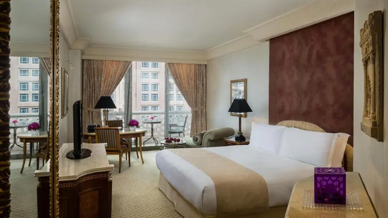 Chambre lumineuse avec un lit double, un coin repas et un fauteuil.