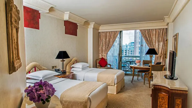 Chambre avec deux lits et vue sur la ville à travers de grandes fenêtres.