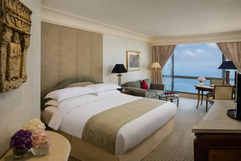 Chambre lumineuse avec un grand lit et un coin salon près d'une fenêtre offrant une vue sur la mer.