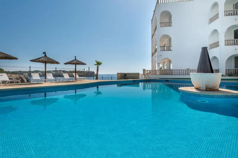 Piscine bleue bordée de chaises longues et de parasols, avec une vue sur la mer.