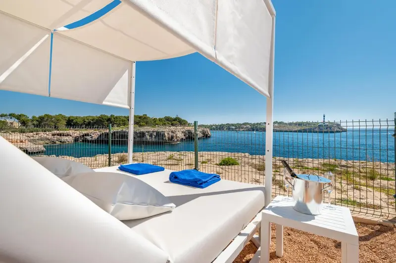 Transats blancs sous un auvent sur une terrasse ensoleillée avec vue sur la mer.