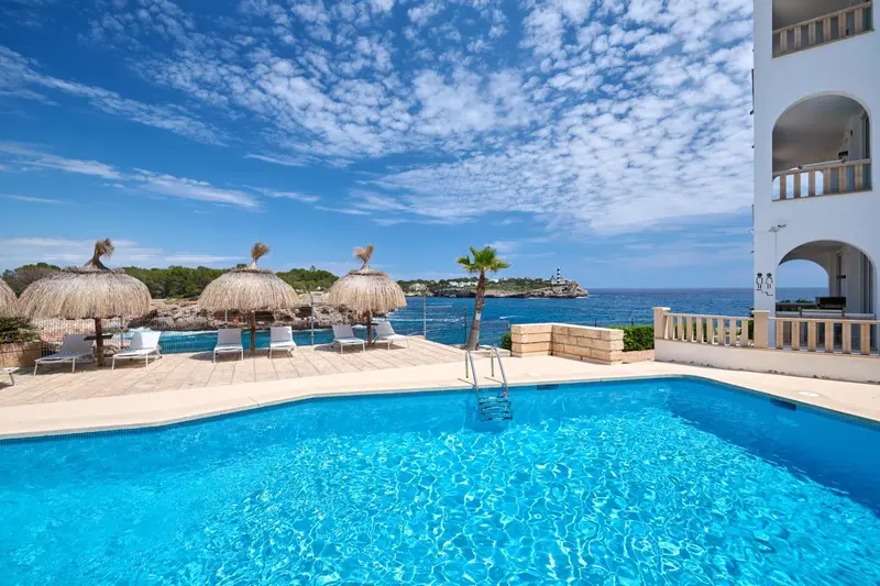 Une piscine bleu turquoise avec des transats et des parasols en bord de mer.