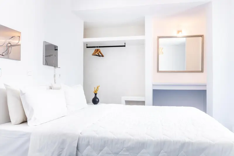 Une chambre lumineuse avec un grand lit recouvert d'une couette blanche et un espace rangement mural.