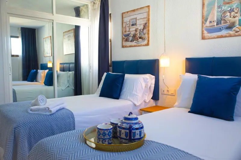 Une chambre lumineuse avec un grand lit recouvert d'une courtepointe bleue et de coussins.