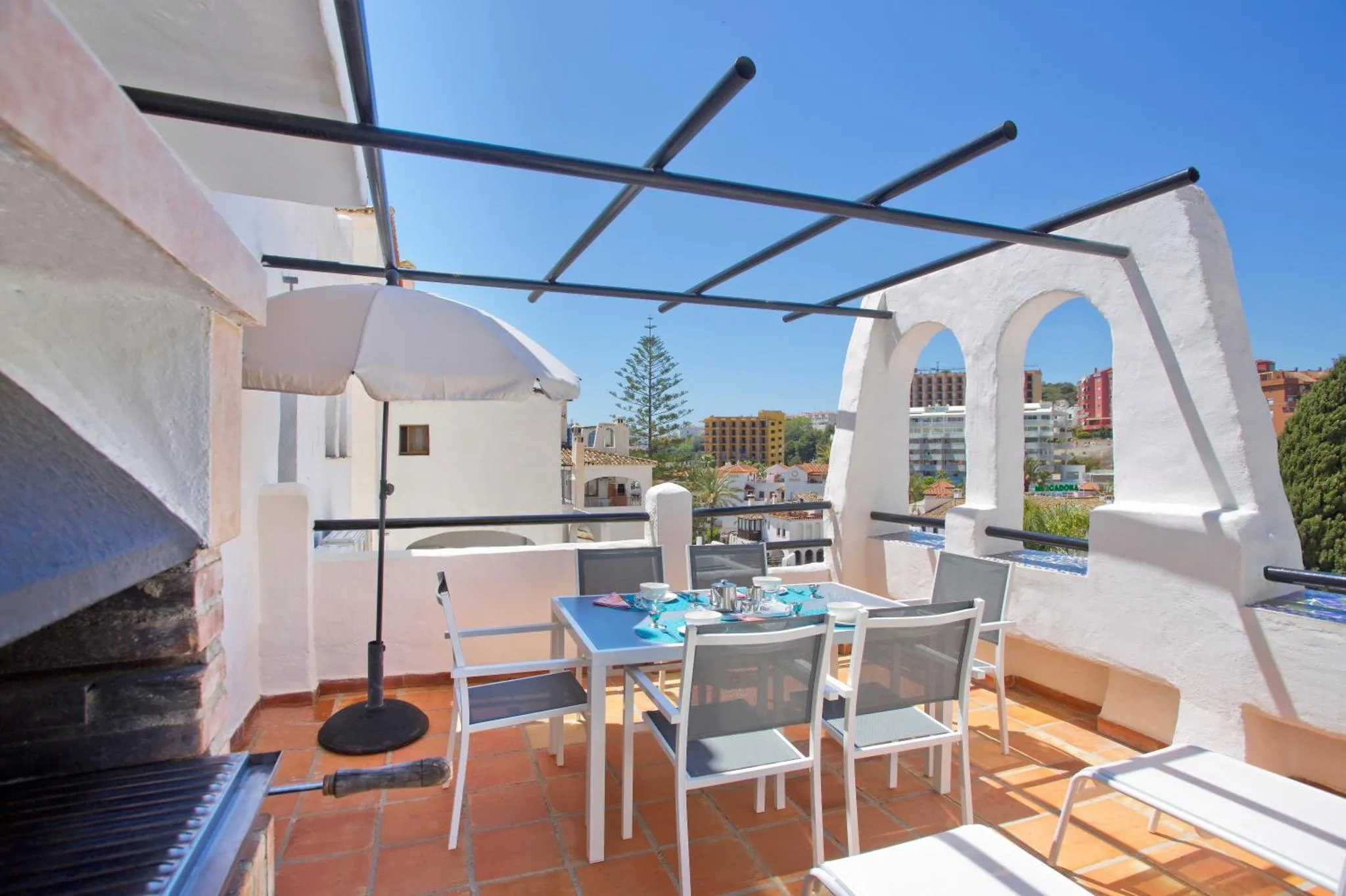 Une table et des chaises sont disposées sur une terrasse ombragée avec vue sur la ville.