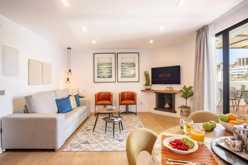 Un salon clair avec canapé, fauteuils et table basse, donnant sur une terrasse.