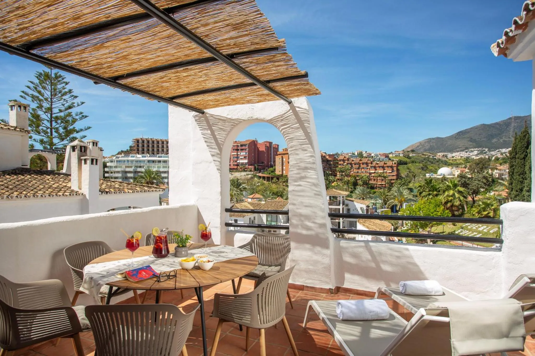 Table et chaises sur une terrasse ombragée avec vue sur la ville et les montagnes.