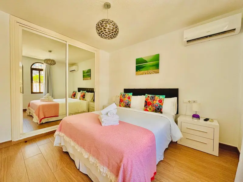 Une chambre lumineuse avec un grand lit recouvert d'une courtepointe rose et de coussins colorés.