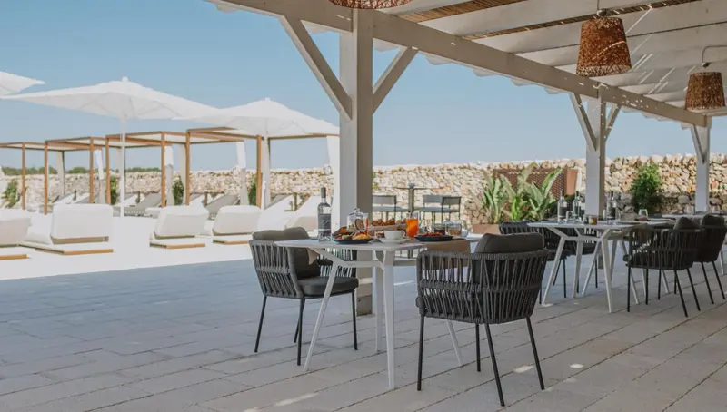 Une table est dressée pour un repas en extérieur, sous une structure ombragée.