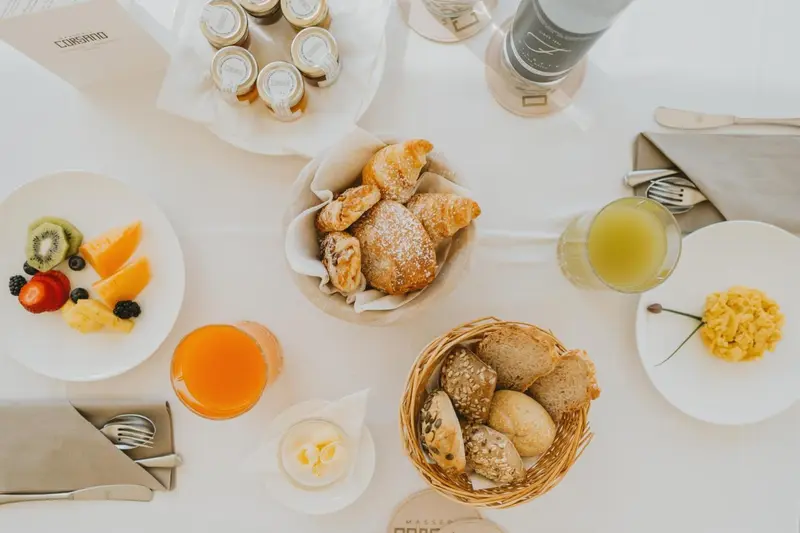 Une table blanche est dressée avec un petit-déjeuner composé de viennoiseries, de fruits frais, de jus d'orange et d'œufs brouillés.
