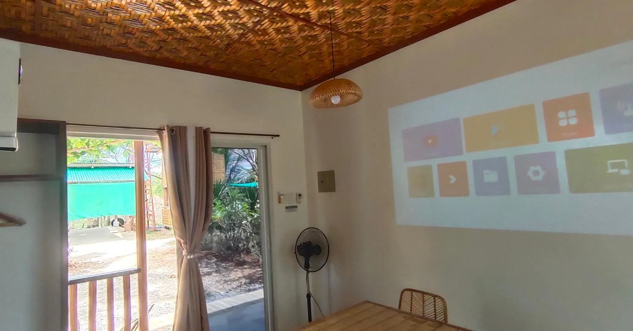 Une pièce lumineuse avec une table et un ventilateur, donnant sur une terrasse ombragée.
