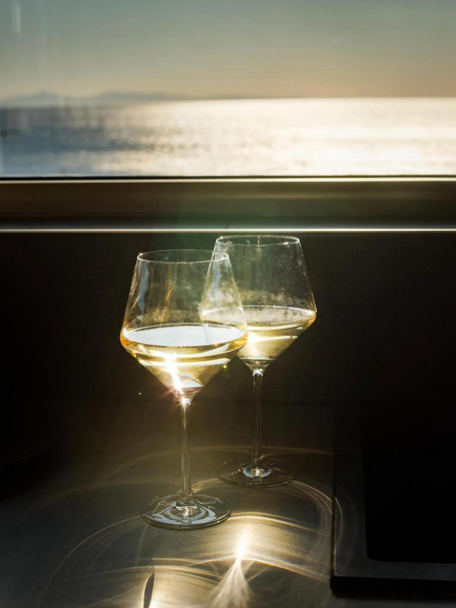 Deux verres de vin sur une table sombre avec vue sur la mer scintillante.