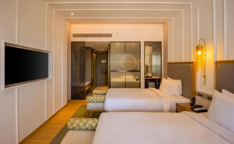 Chambre lumineuse avec deux lits simples et un téléviseur mural.
