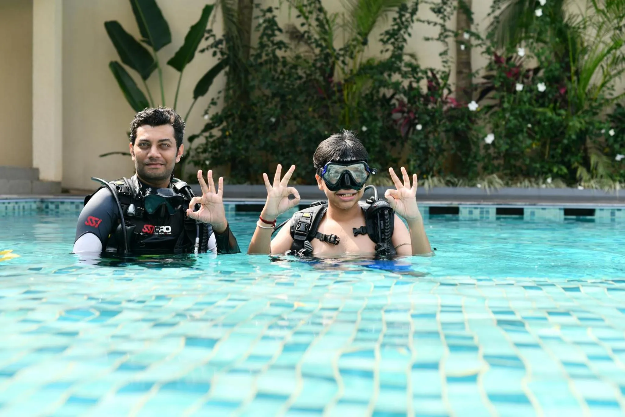 Deux personnes souriantes en gilets stabilisateurs et masque dans une piscine.