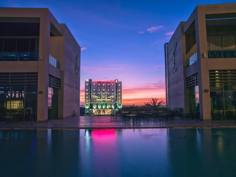 Façade d'un bâtiment moderne illuminé au crépuscule, avec une piscine au premier plan.