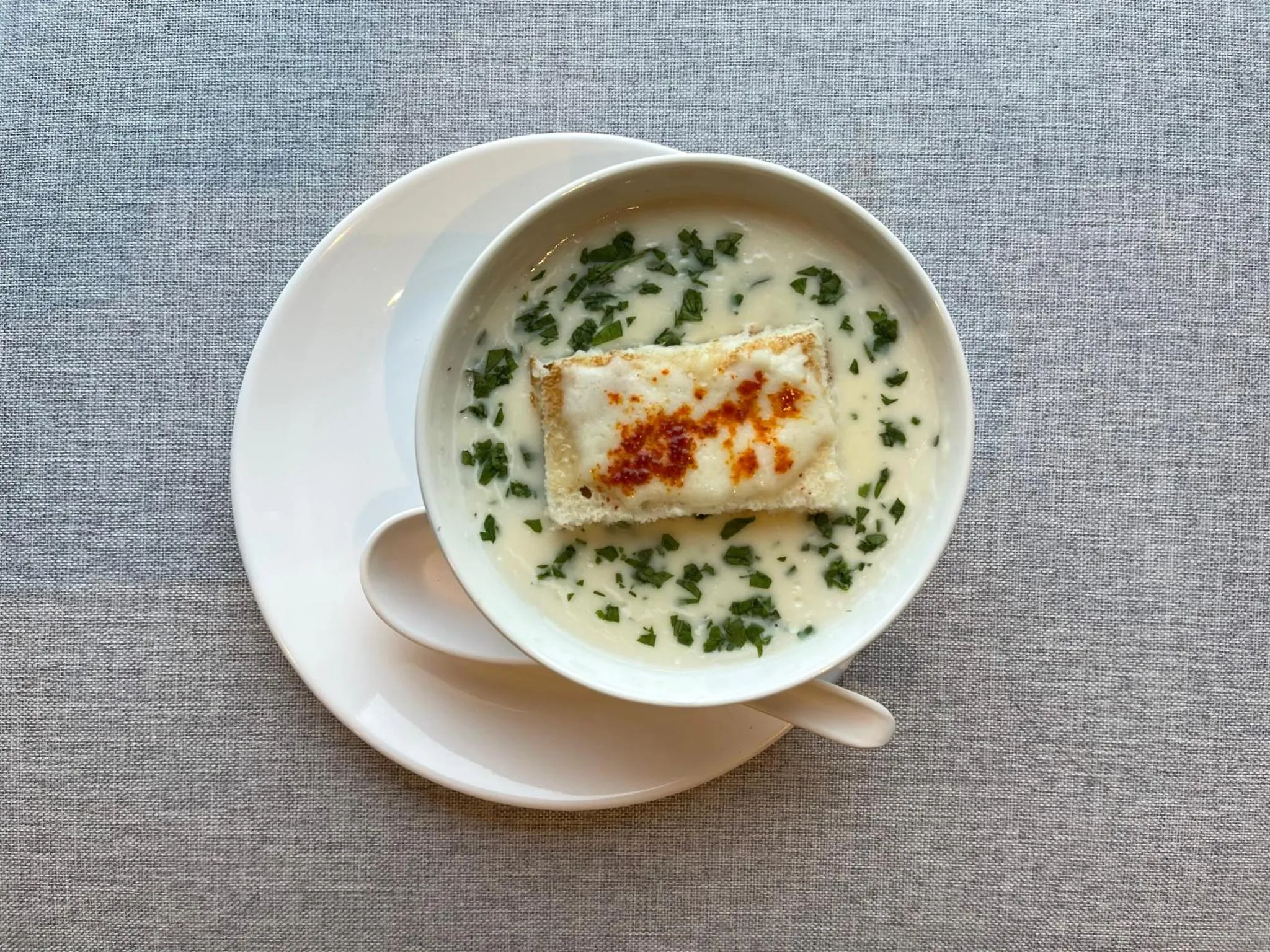 Une soupe crémeuse blanche avec des herbes et des croûtons gratinés.