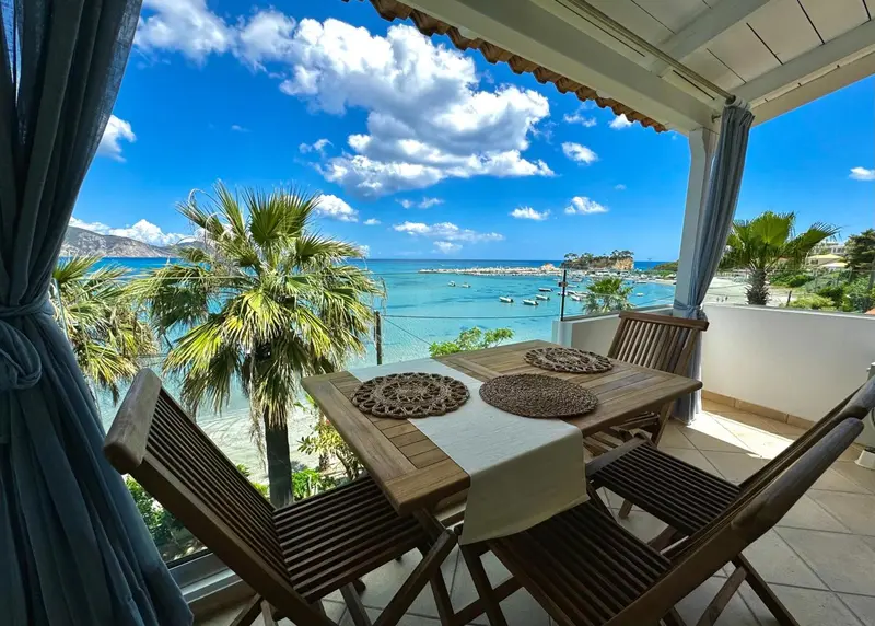 Table et chaises en bois sur une terrasse ensoleillée avec vue sur la mer.
