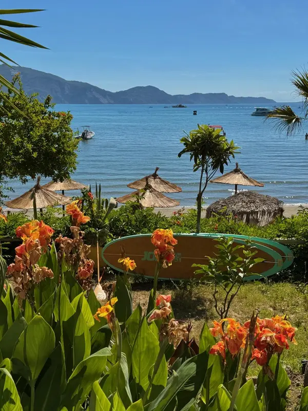 Plage de sable fin avec parasols de chaume et végétation tropicale en premier plan.