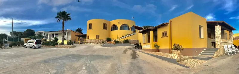 Bâtiment jaune à l'architecture arrondie avec un palmier et un parking en contrebas.