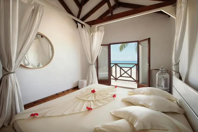 Une chambre lumineuse avec un lit recouvert de pétales de fleurs donnant sur une vue mer.