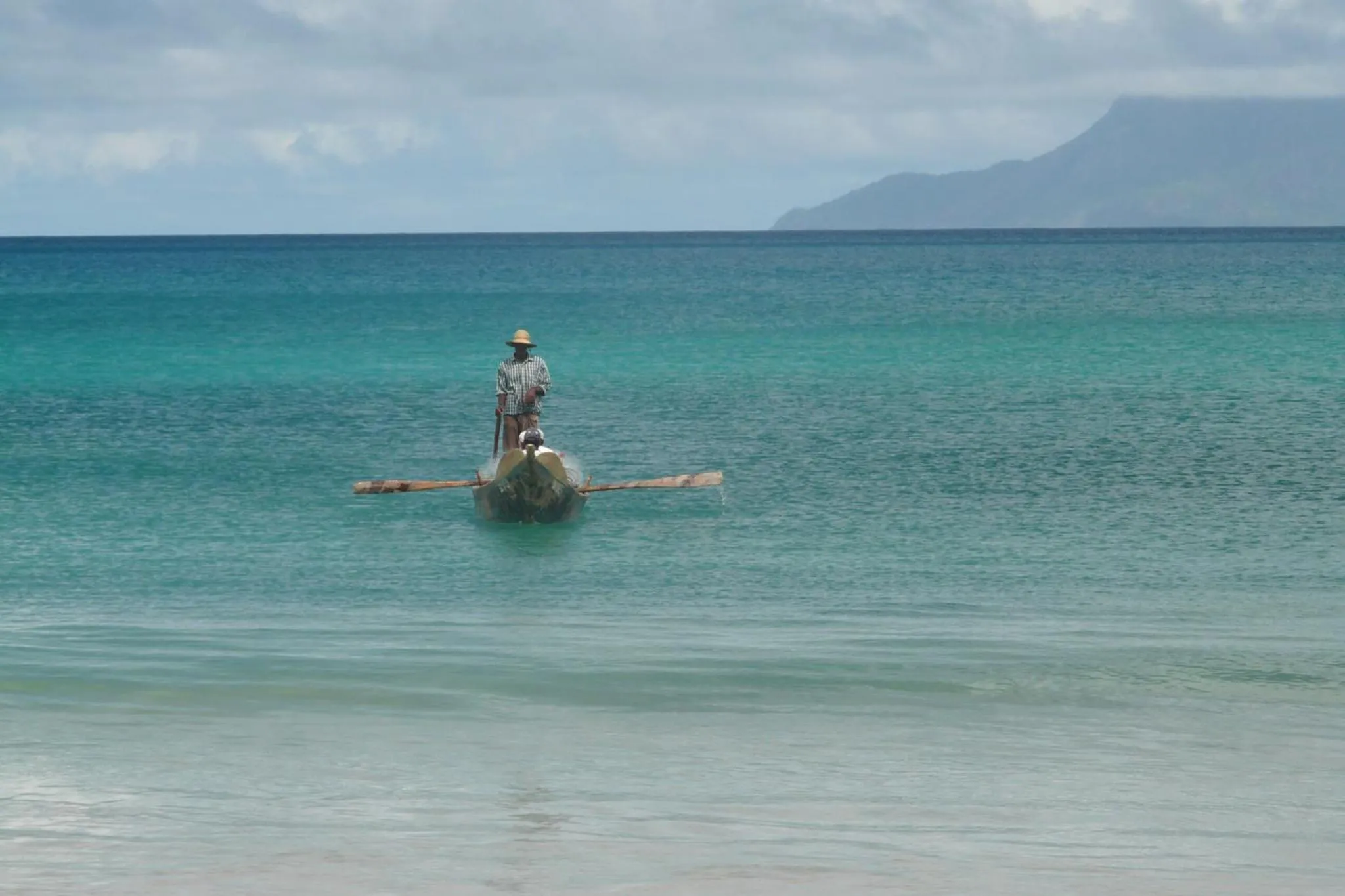 Une personne rame sur une pirogue dans une eau turquoise.