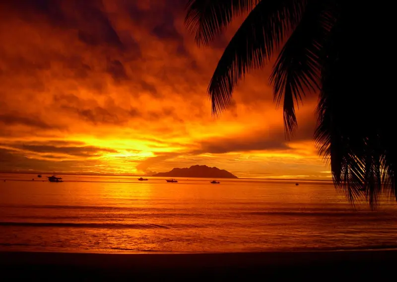 Coucher de soleil flamboyant sur une mer calme avec des embarcations à l'horizon.
