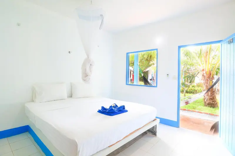 Une chambre lumineuse avec un lit recouvert d'une courtepointe bleue et une porte ouverte sur une végétation tropicale.