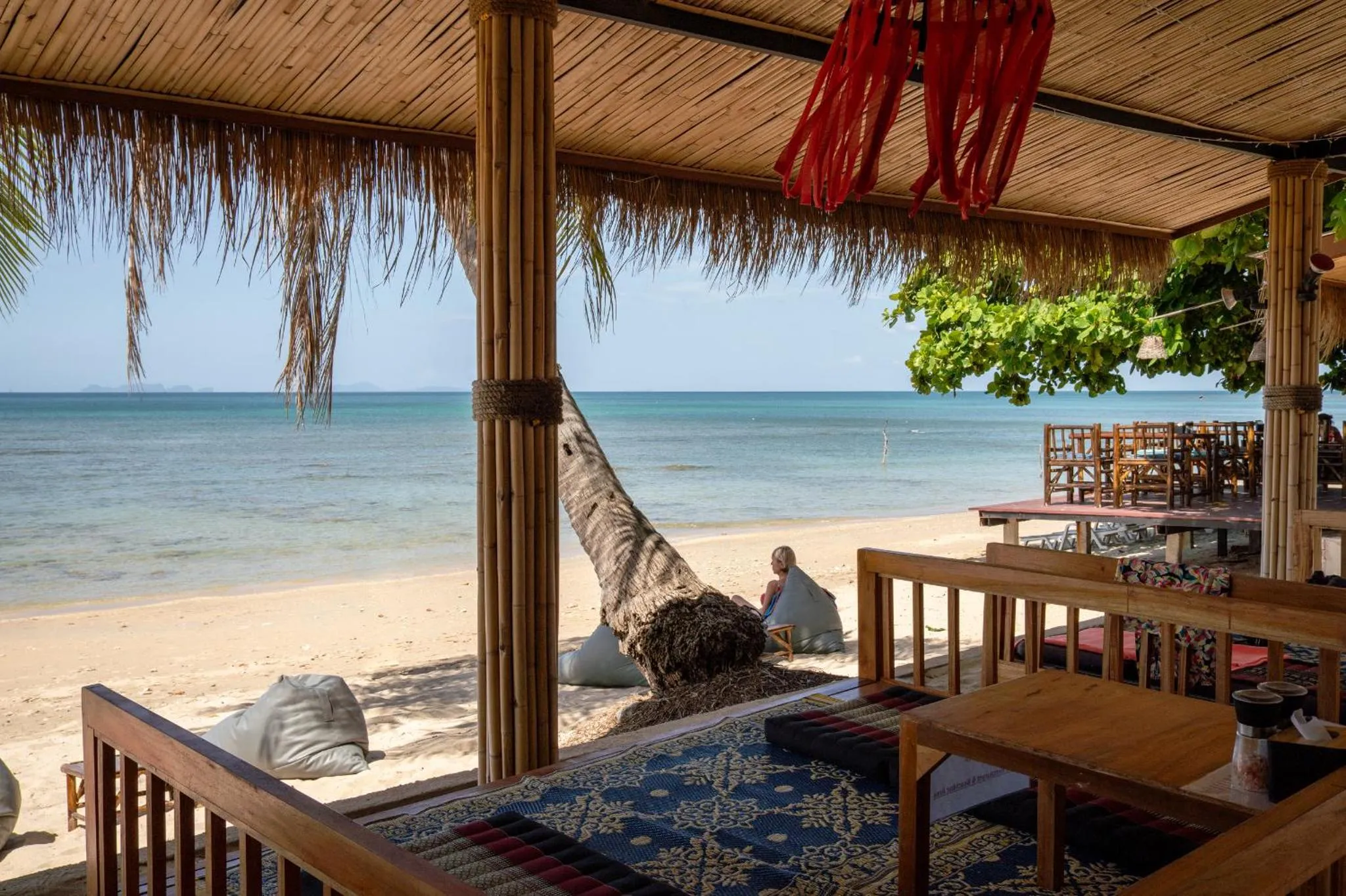 Espace de détente ombragé donnant sur une plage de sable fin et la mer.