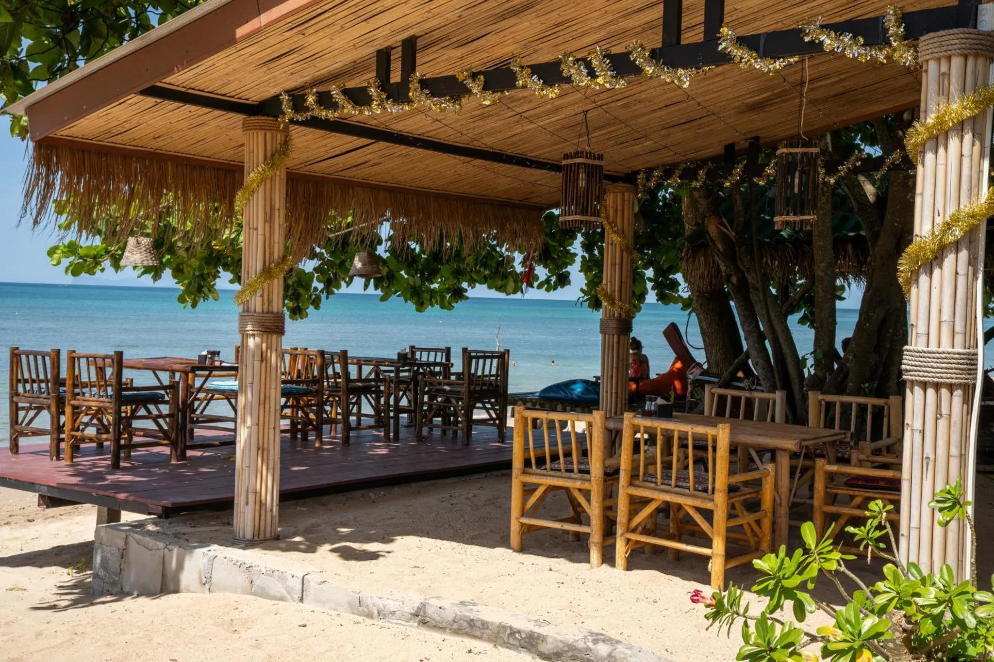 Terrasse ombragée avec tables et chaises en bois face à la mer.