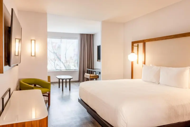 Chambre lumineuse avec un lit double et un coin salon près de la fenêtre.