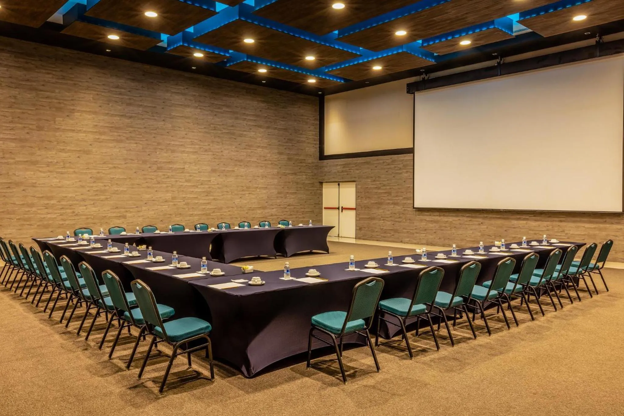 Une grande salle de réunion est aménagée avec des tables et des chaises disposées en U.
