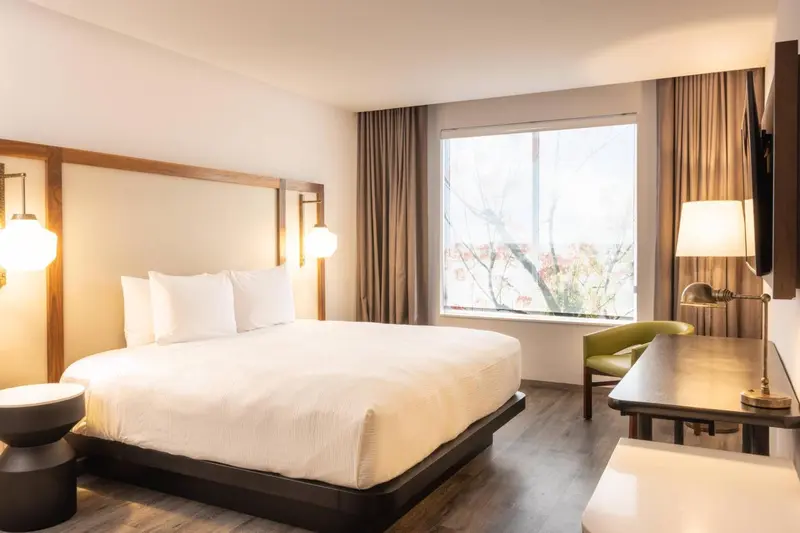Une chambre lumineuse avec un grand lit et un bureau près de la fenêtre.
