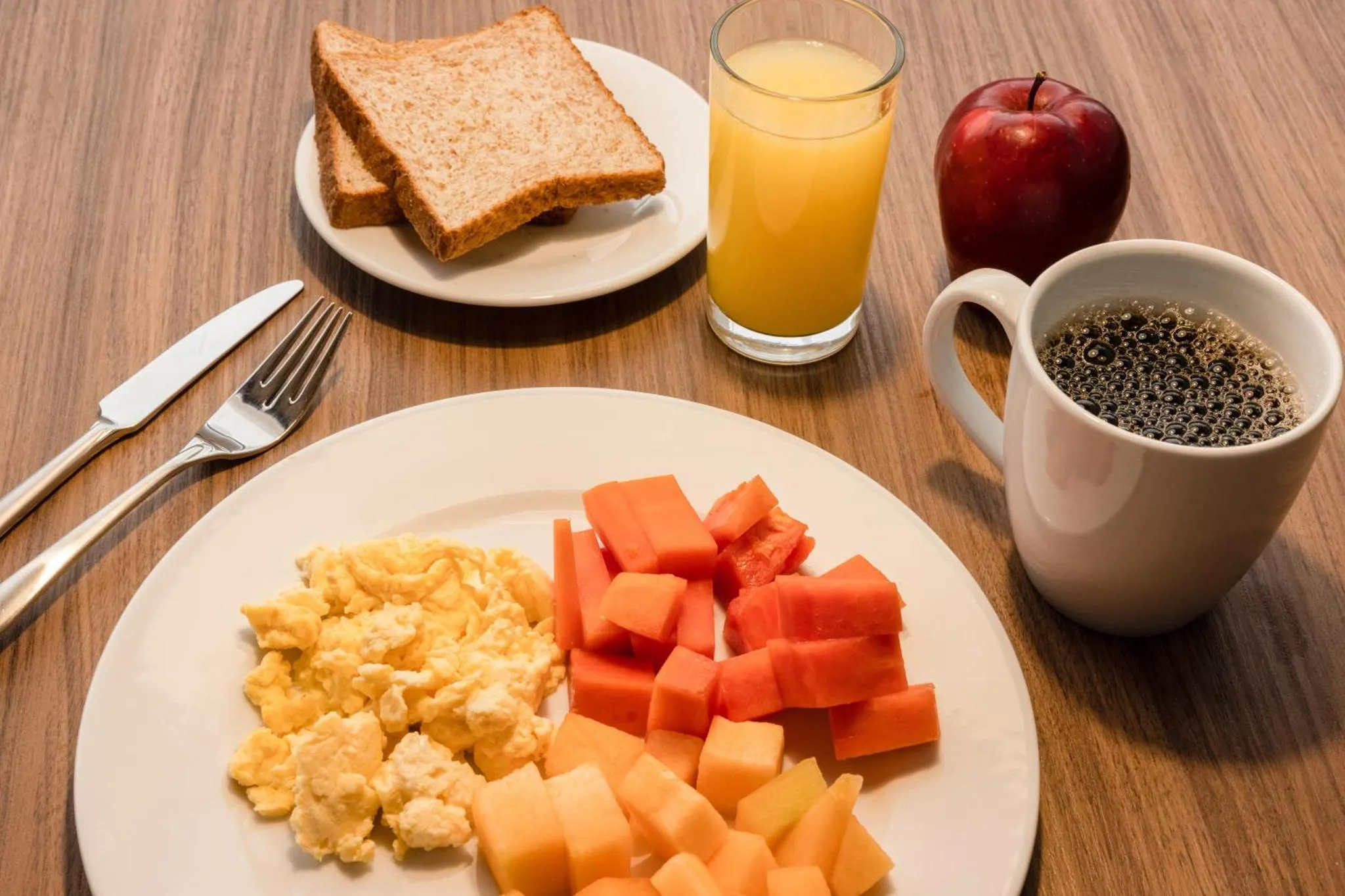 Un petit-déjeuner avec des œufs brouillés, des fruits et des boissons est présenté sur une table.
