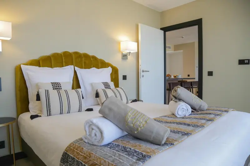 Une chambre lumineuse avec un grand lit recouvert d'oreillers et de coussins décoratifs.