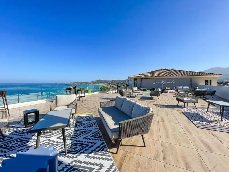 Terrasse aménagée avec canapés, tables basses et chaises, offrant une vue sur la mer.
