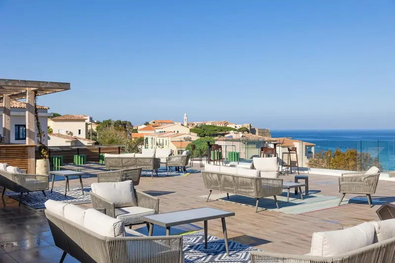 Terrasse aménagée avec des salons de jardin et une vue sur la mer et un village.