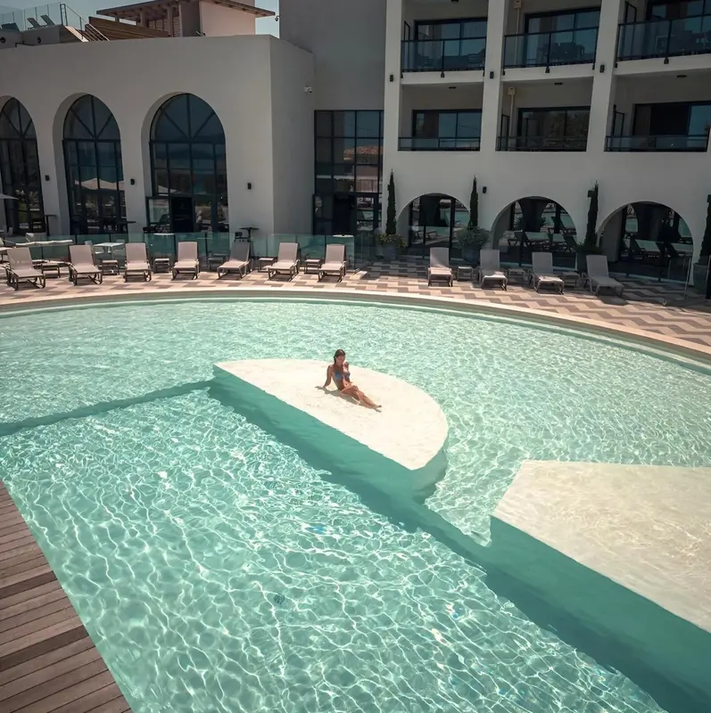 Une personne se relaxe sur une structure blanche au centre d'une piscine turquoise.