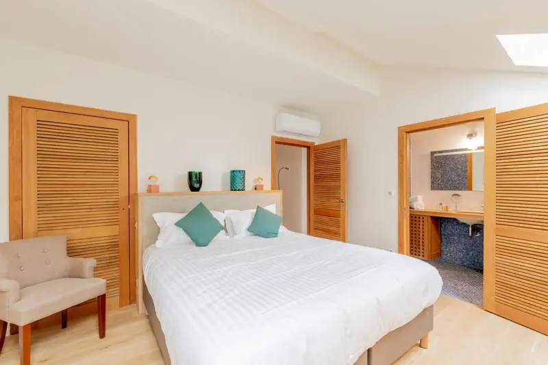 Une chambre lumineuse avec un lit fait et un accès à une salle de bain.