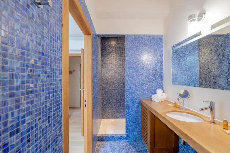 Une salle de bain moderne avec des murs recouverts de mosaïque bleue et un meuble lavabo en bois.