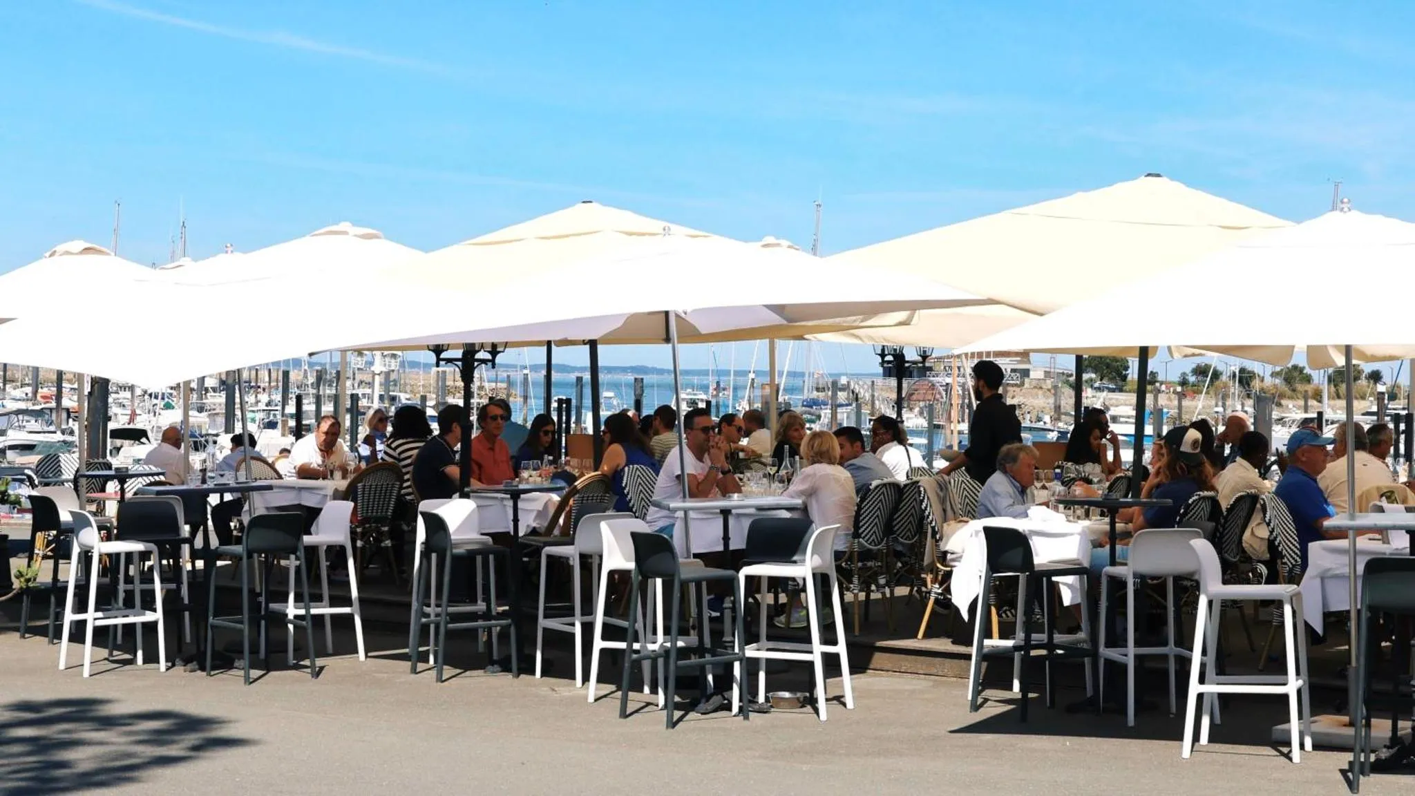 Terrasse ombragée avec tables et chaises en bord de mer.