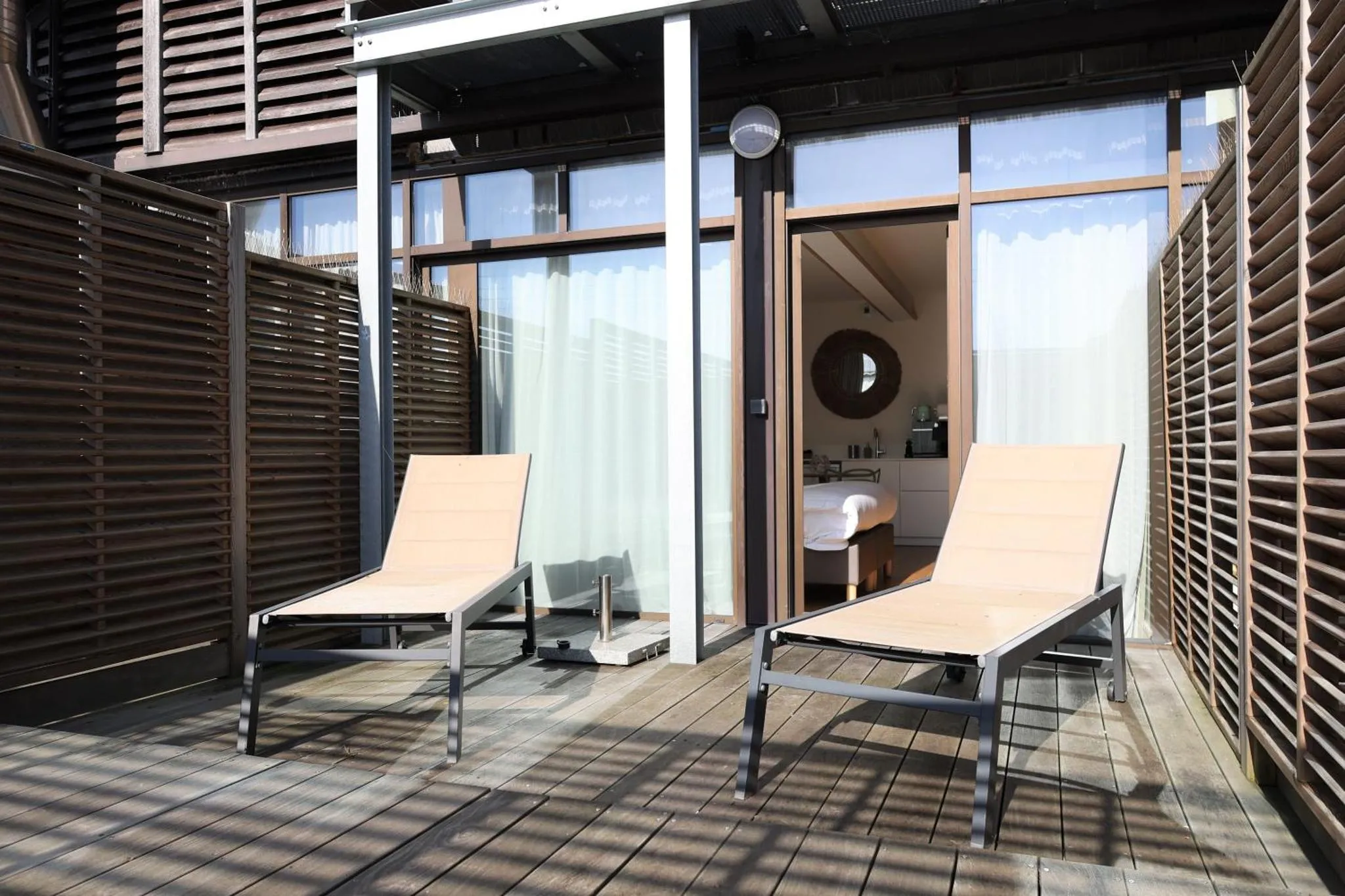 Deux transats sur une terrasse en bois devant une baie vitrée.