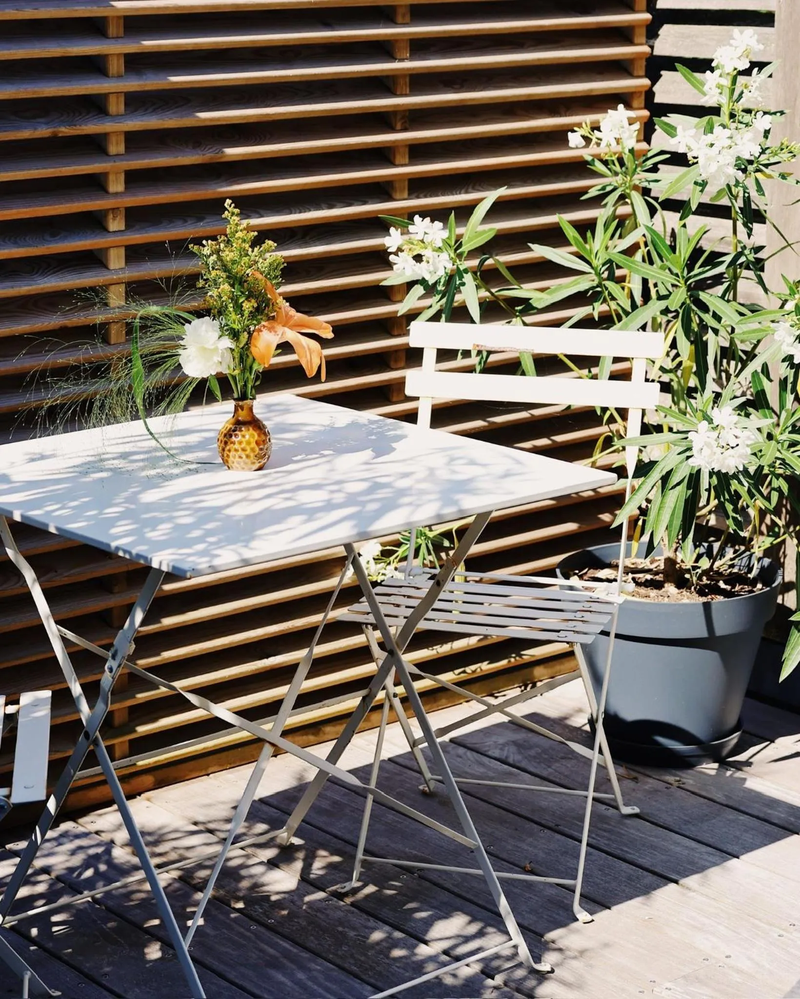 Une table et une chaise blanches sur une terrasse en bois ombragée.
