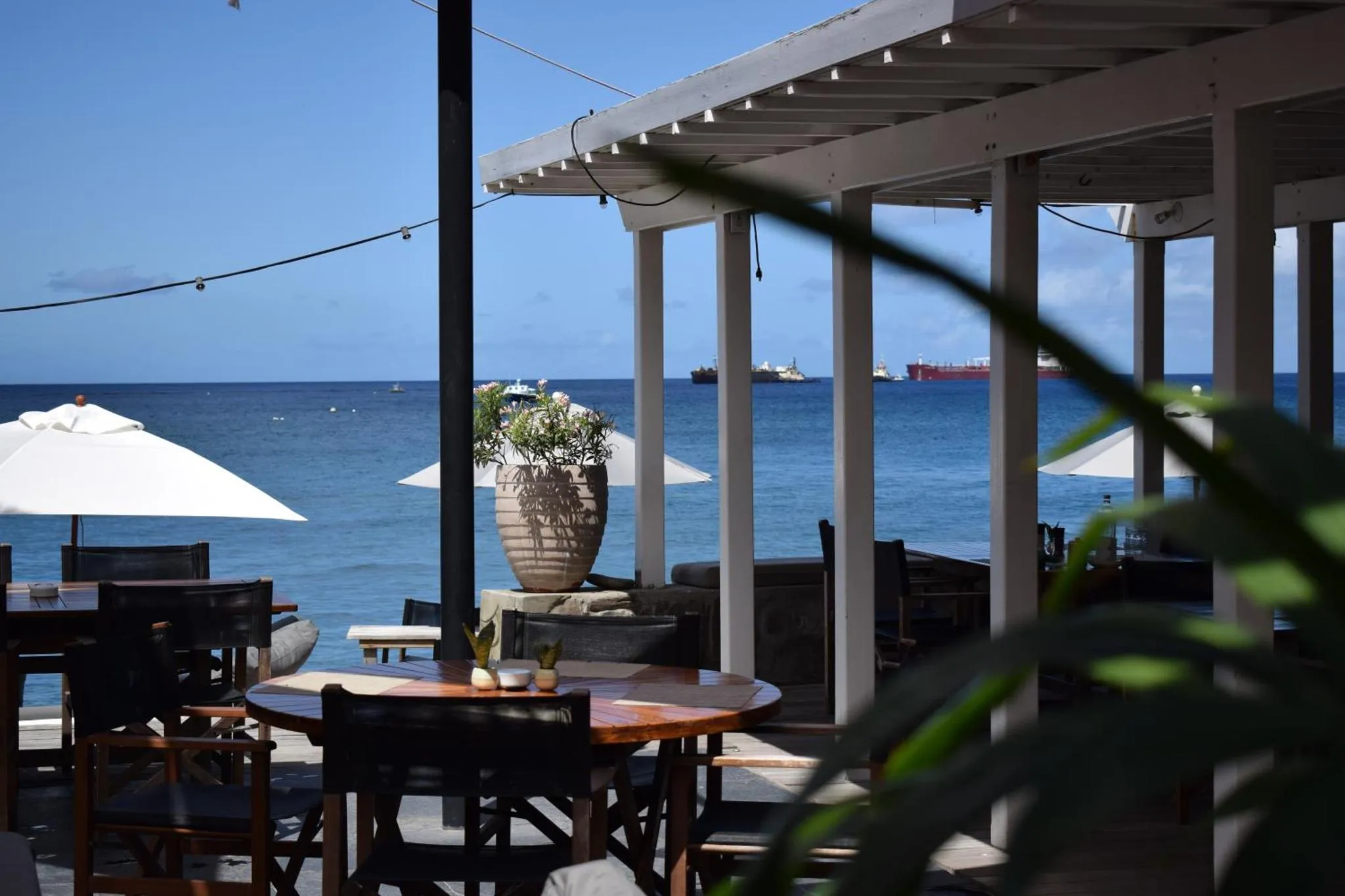 Tables et chaises disposées sur une terrasse ombragée face à la mer.