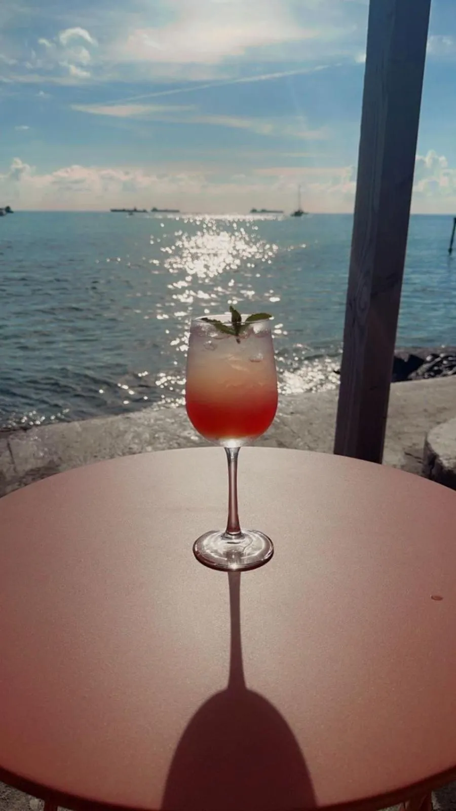 Un cocktail coloré est posé sur une table ronde face à la mer.