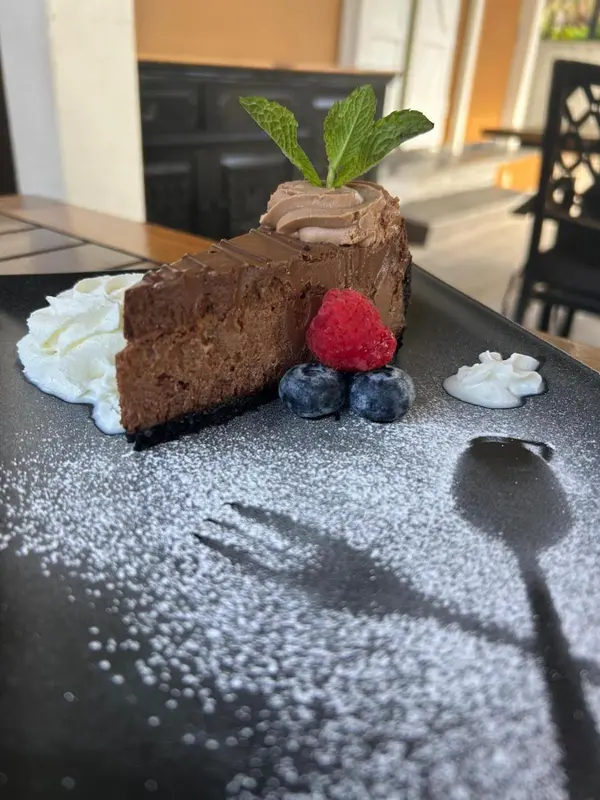 Une part de gâteau au chocolat est présentée sur une assiette noire décorée de crème et de fruits rouges.