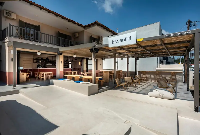 Terrasse ombragée avec tables et chaises devant un bâtiment blanc.