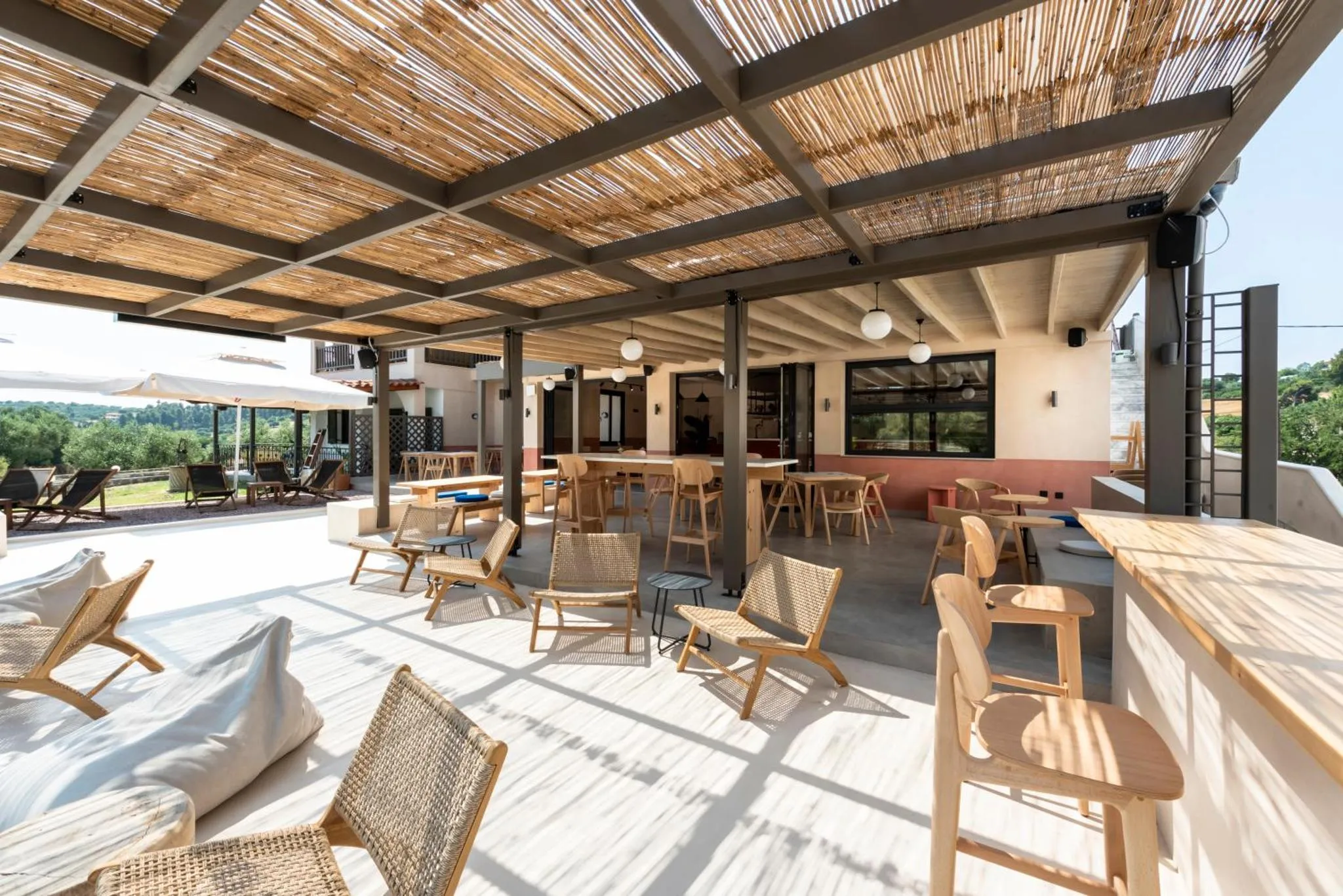 Terrasse ombragée avec tables et chaises en bois, vue sur la végétation.