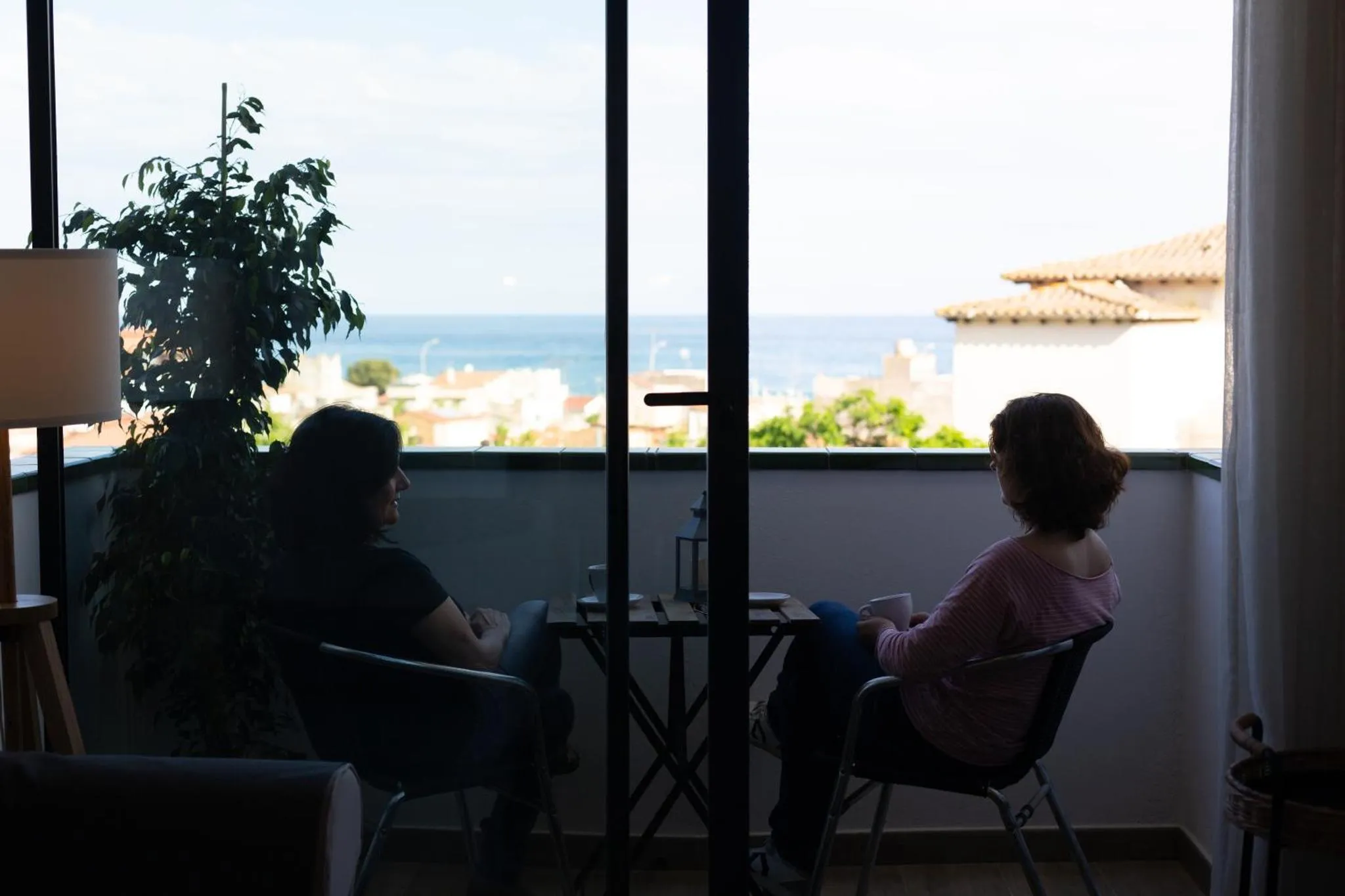 Deux personnes sont assises à une table devant une grande baie vitrée donnant sur la mer et la ville.