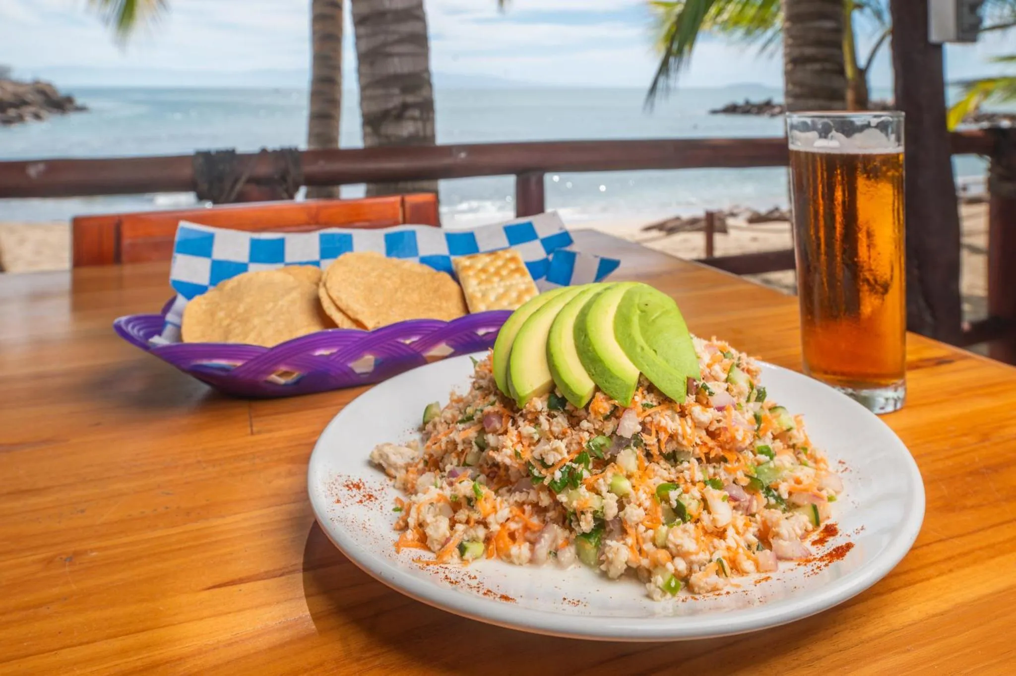 Assiette de ceviche et verre de bière sur une table en bois face à la mer.
