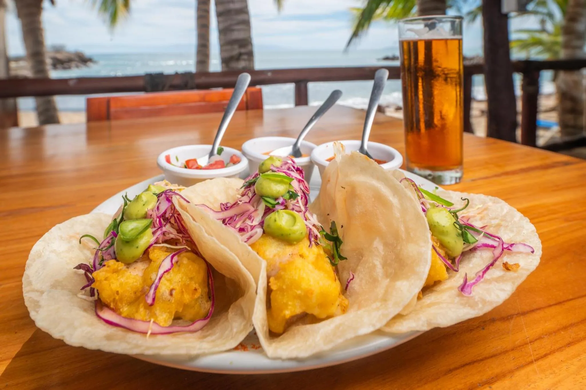 Assiette de tacos garnis sur une table en bois avec une boisson rafraîchissante en arrière-plan.